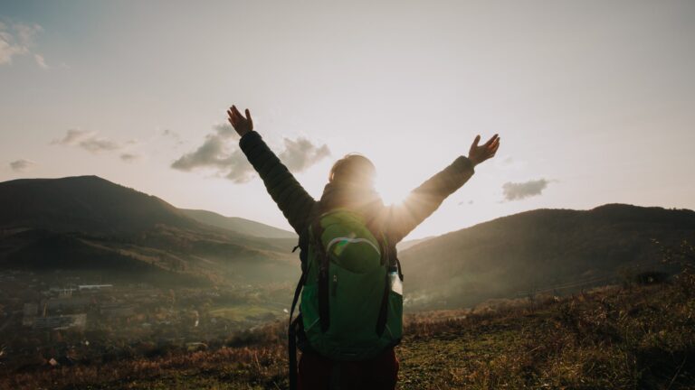 Picture of a woman on top of a mountain raising their arms in celebration at their achievement