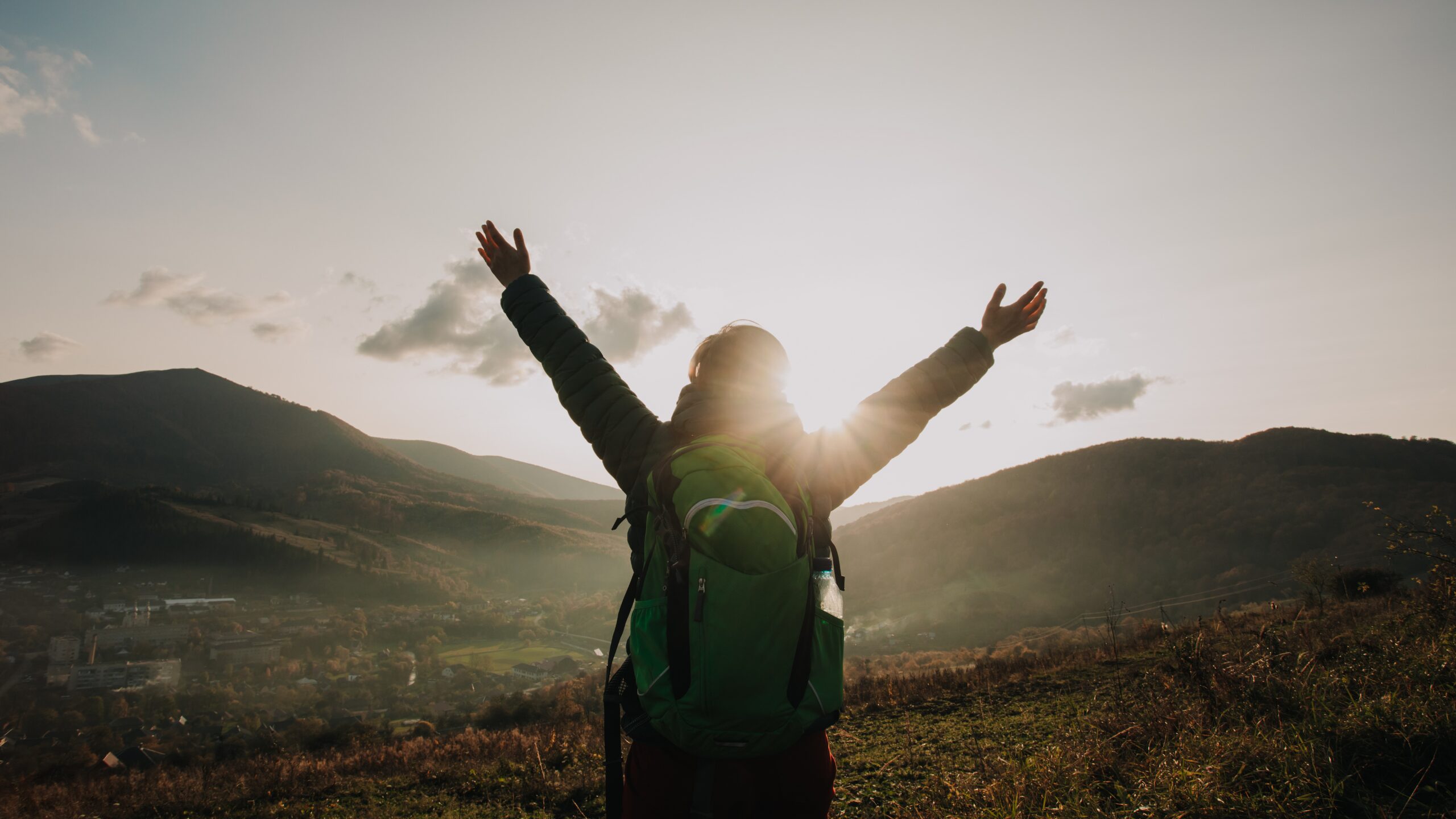 Picture of a woman on top of a mountain raising their arms in celebration at their achievement